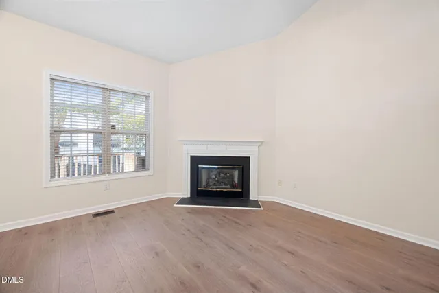 an empty room with wooden floor fireplace and windows