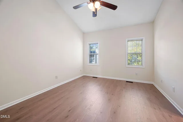 an empty room with wooden floor cabinet and windows