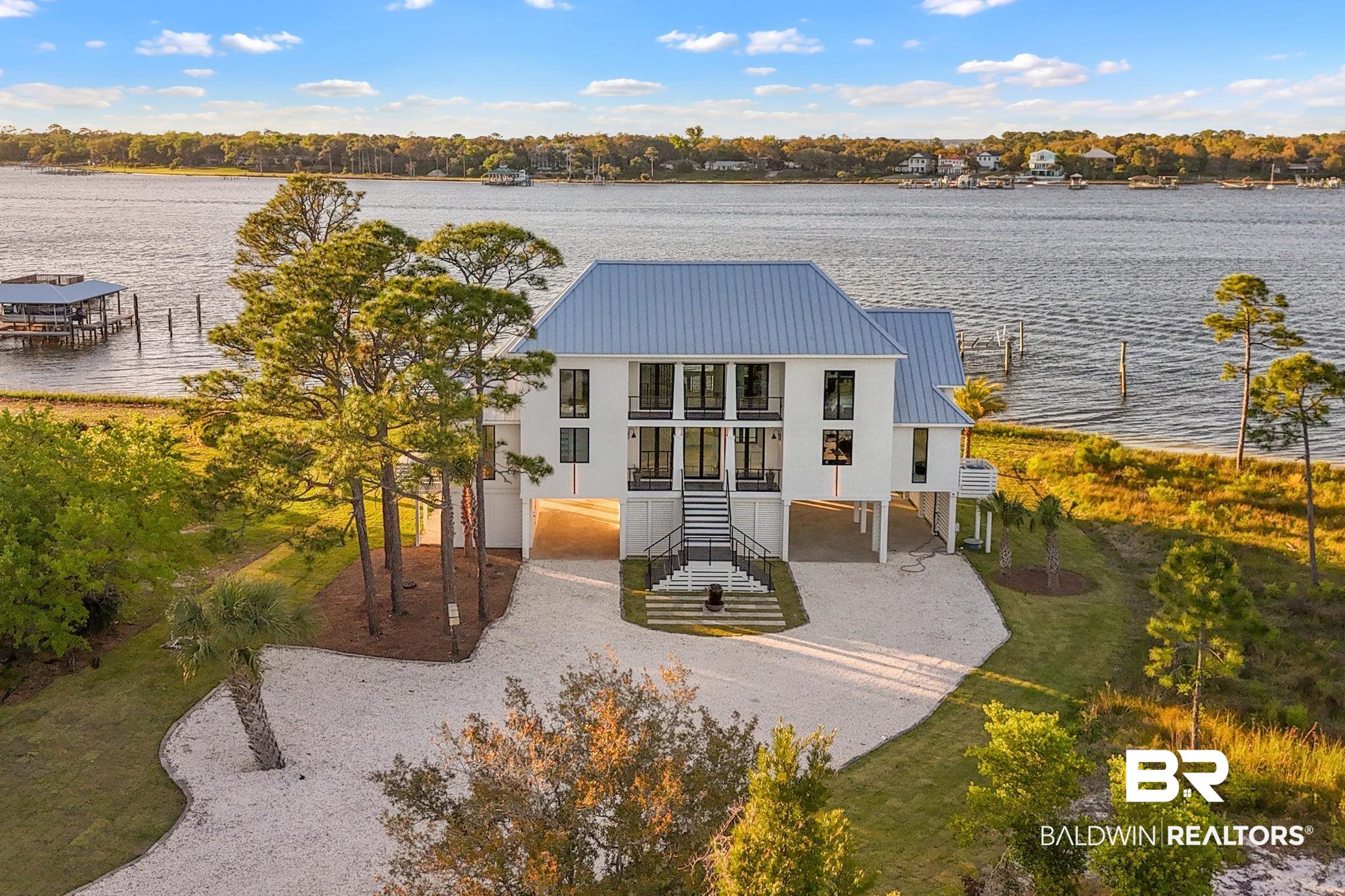 33349 River Road Orange Beach, AL 36561 - Photo 51 of 61 Waterfront residence featuring a white exterior, metal roof, elevated foundation, multiple balconies, and a gravel driveway