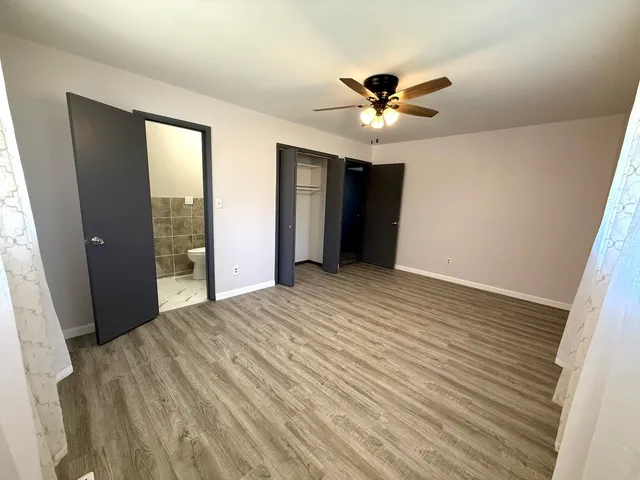 a view of an empty room with wooden floor and a ceiling fan