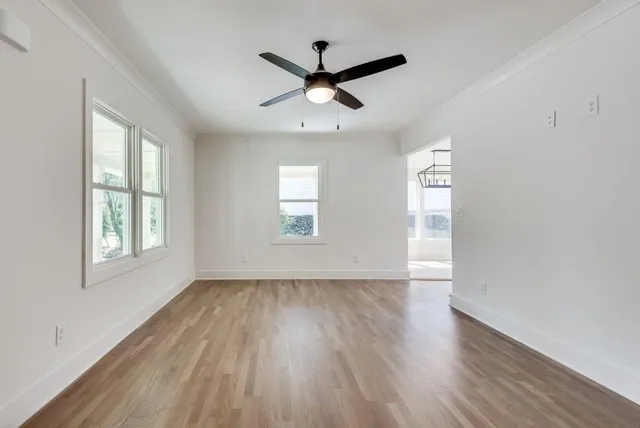 an empty room with wooden floor a ceiling fan and windows