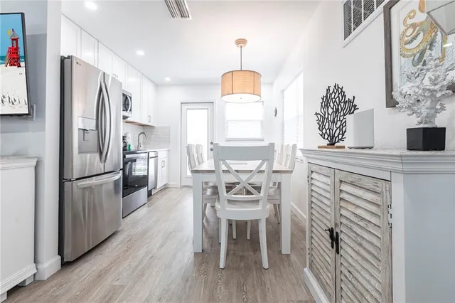 a kitchen with stainless steel appliances a refrigerator a stove a dining table and chairs with wooden floor