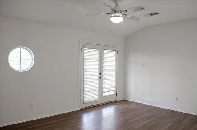 an empty room with wooden floor chandelier fan and windows