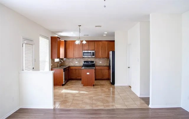 a kitchen with stainless steel appliances kitchen island granite countertop a refrigerator a sink dishwasher a stove and a refrigerator with wooden floor