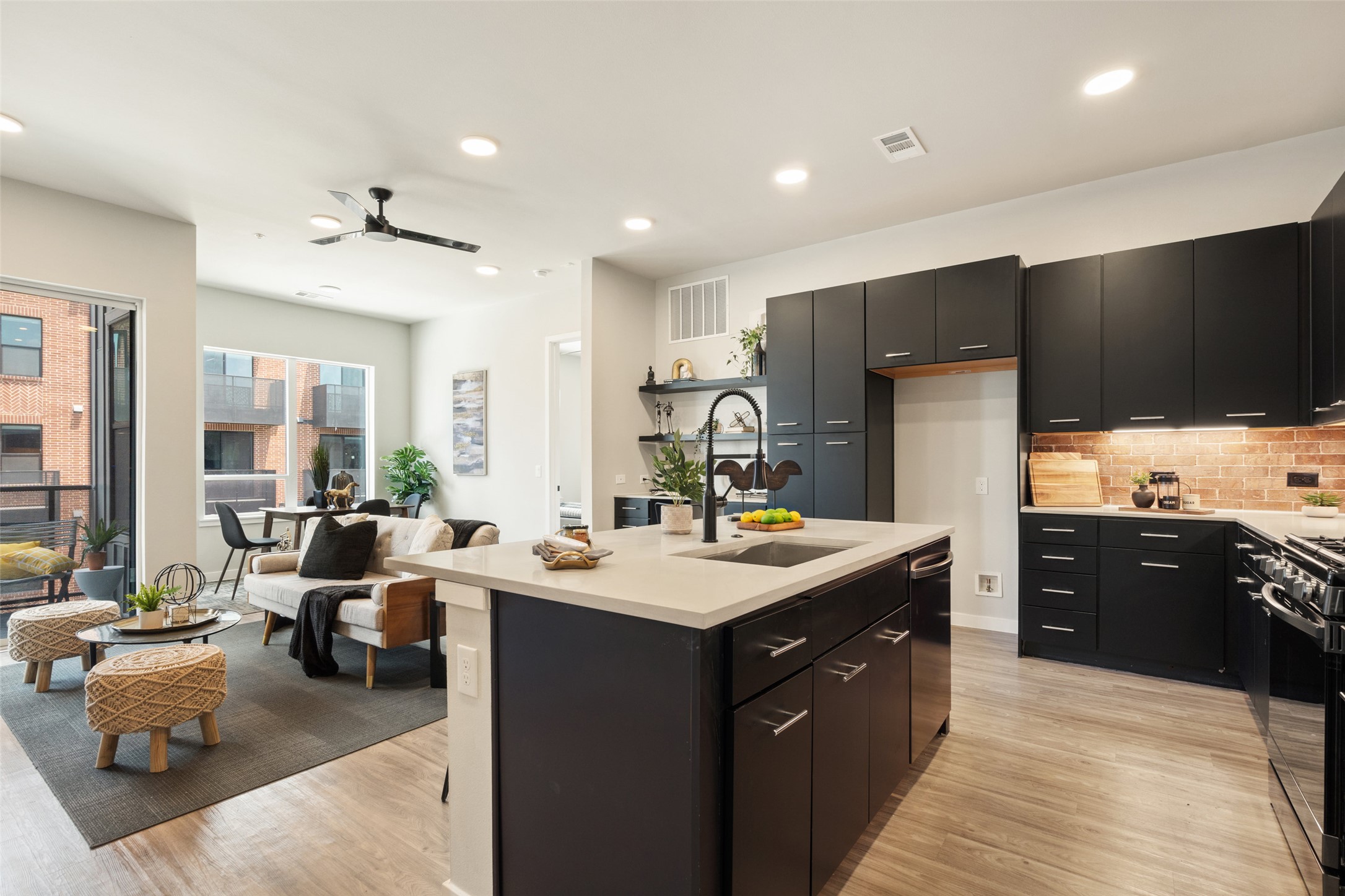 4510 Terry-O Lane, Unit 341 Austin, TX 78745 - Photo 9 of 40 Open concept living space featuring a kitchen with dark cabinetry, a light-colored island with an integrated sink, and an exposed brick backsplash