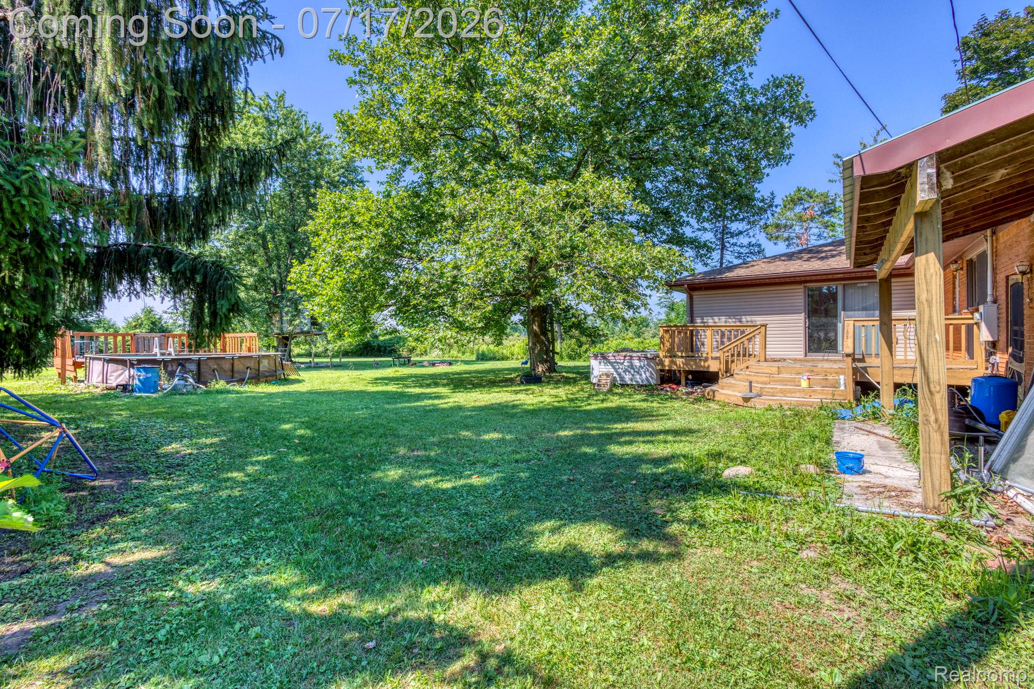 9805 Dolan Road Columbus, MI 48063 - Photo 29 of 39 Spacious backyard featuring an above-ground pool with surrounding wood decking, mature trees, and a wooden porch with railing