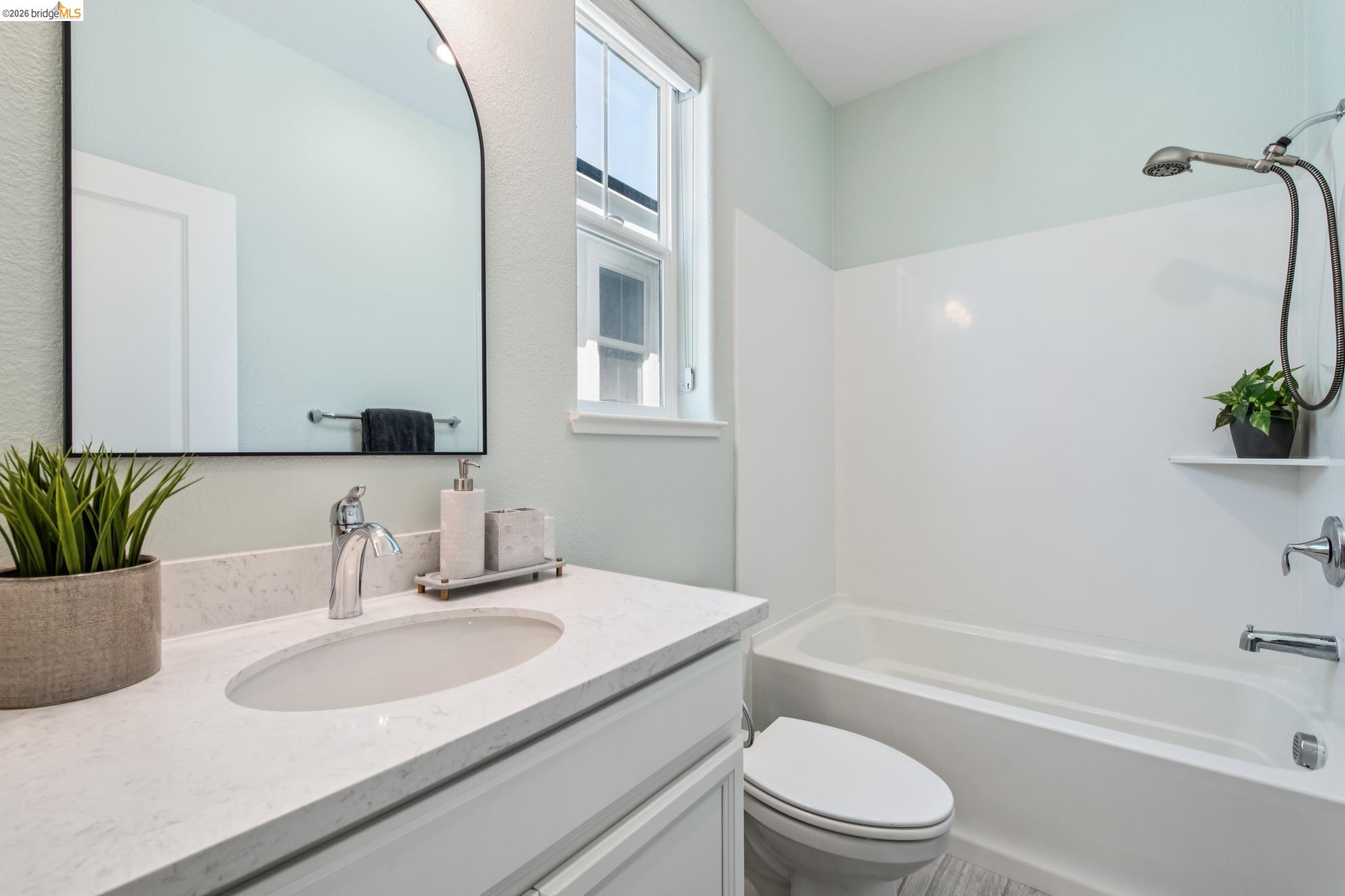 24157 Amaranth Loop Hayward, CA 94541 - Photo 47 of 63 Bathroom featuring a light-colored vanity with an integrated sink, a large wall-mounted mirror, a window for natural light, a toilet, and a bathtub with an integrated shower head