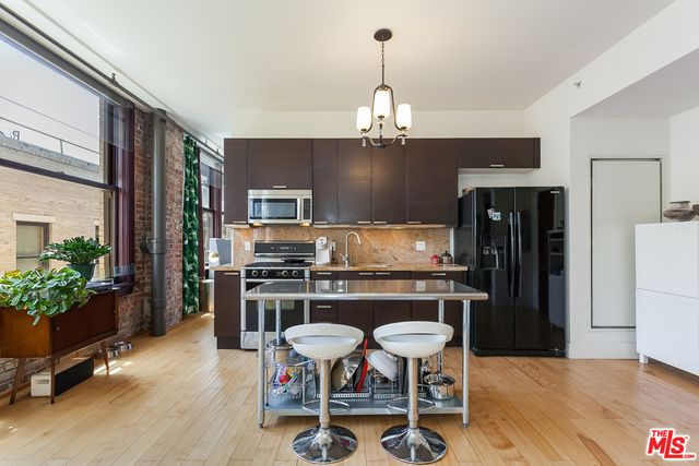 a kitchen with stainless steel appliances granite countertop a stove top oven a refrigerator a stove and a dining table with wooden floor