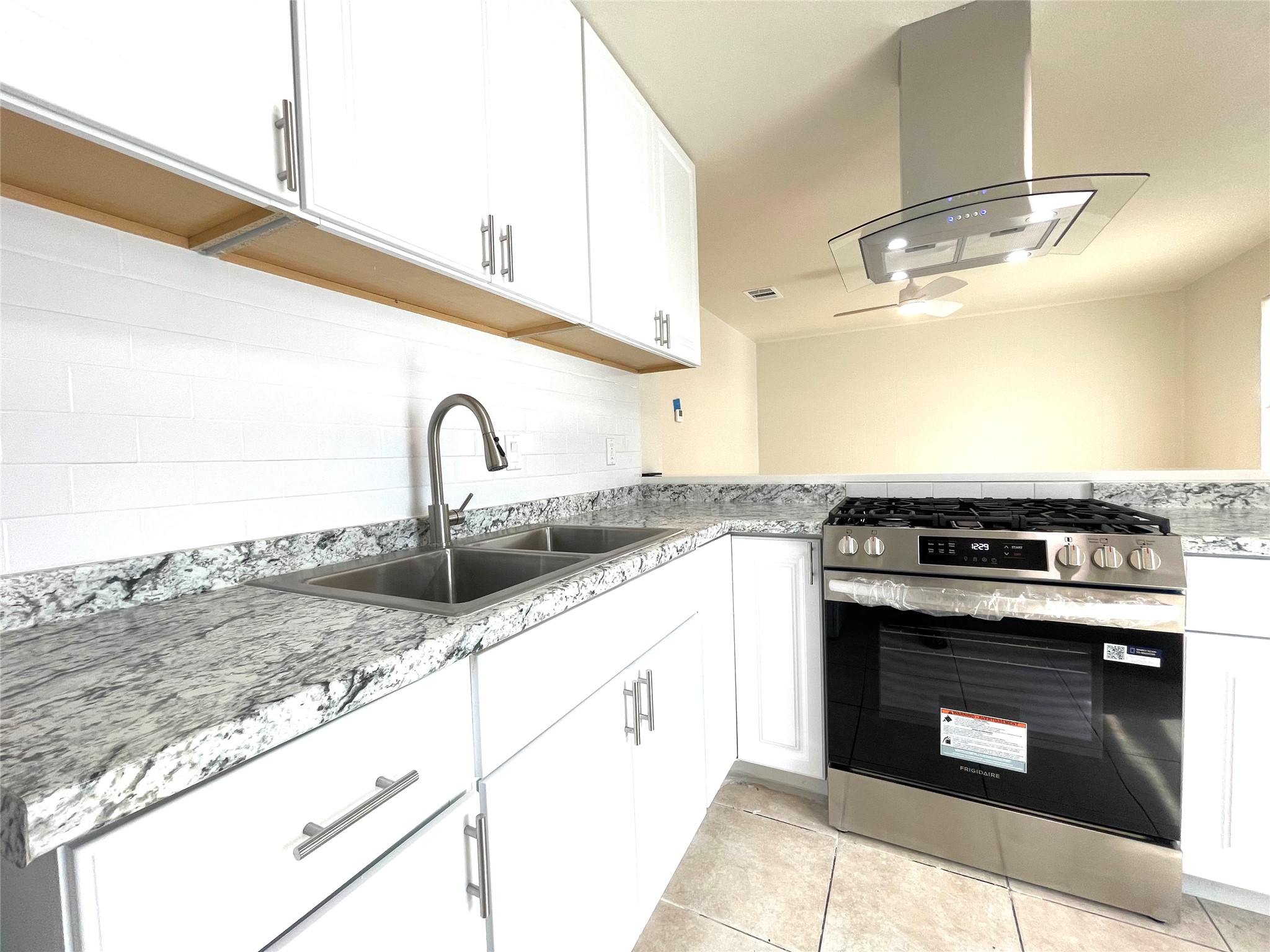 Kitchen with gas stove, island exhaust hood, white cabinets, and light tile patterned floors