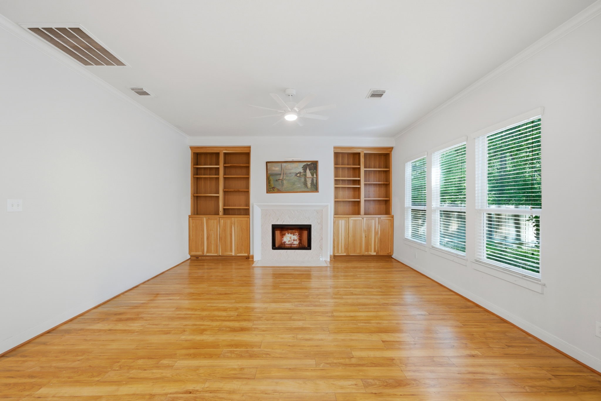 158 Lattice Gate Street Spring, TX 77382 - Photo 3 of 35 Expansive windows fill the living area with abundant natural light, highlighting the warm wood floors and open layout. A central fireplace is flanked by custom built-in shelving, providing a sophisticated focal point for this first-floor living space. Access to the screened-in patio ensures a seamless transition to outdoor relaxation and picturesque backyard views.