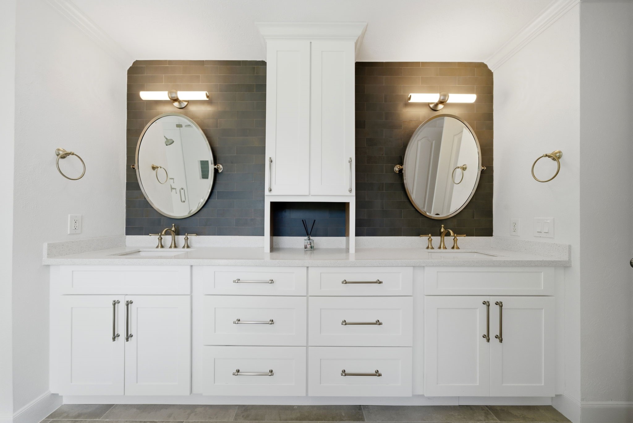 158 Lattice Gate Street Spring, TX 77382 - Photo 6 of 35 Renovated with modern sophistication, the primary bath features a dual sink vanity with crisp white cabinetry and upgraded brass fixtures. Striking dark subway tile backsplashes create a bold contrast against the oval mirrors and central storage tower, while high-end lighting adds a refined touch to this spa-like retreat.