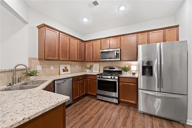 a kitchen with granite countertop wooden floors stainless steel appliances and a counter space