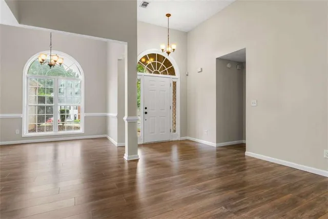 an empty room with wooden floor a chandelier and windows