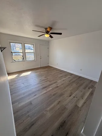 an empty room with wooden floor ceiling fan and windows