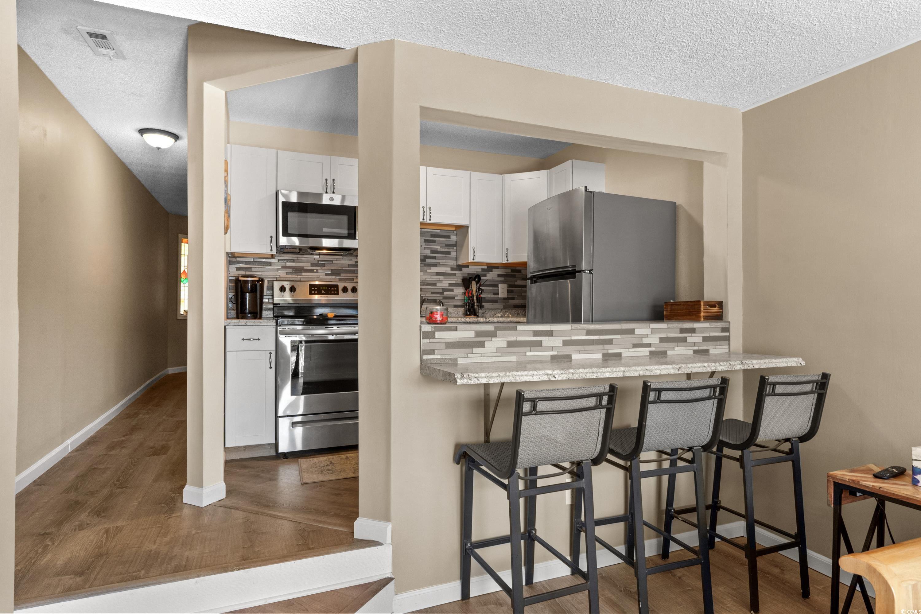 625 North Waccamaw Drive, Unit 107 Murrells Inlet, SC 29576 - Photo 9 of 37 Kitchen with stainless steel appliances, backsplash, white cabinets, dark wood finished floors, and a textured ceiling
