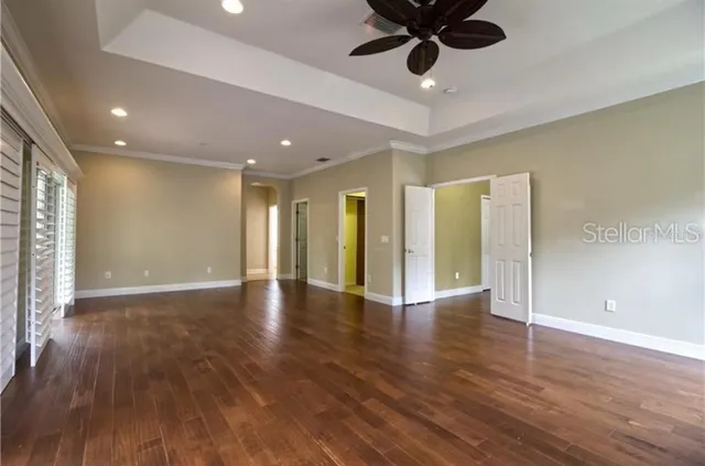 a view of an empty room with wooden floor and a ceiling fan