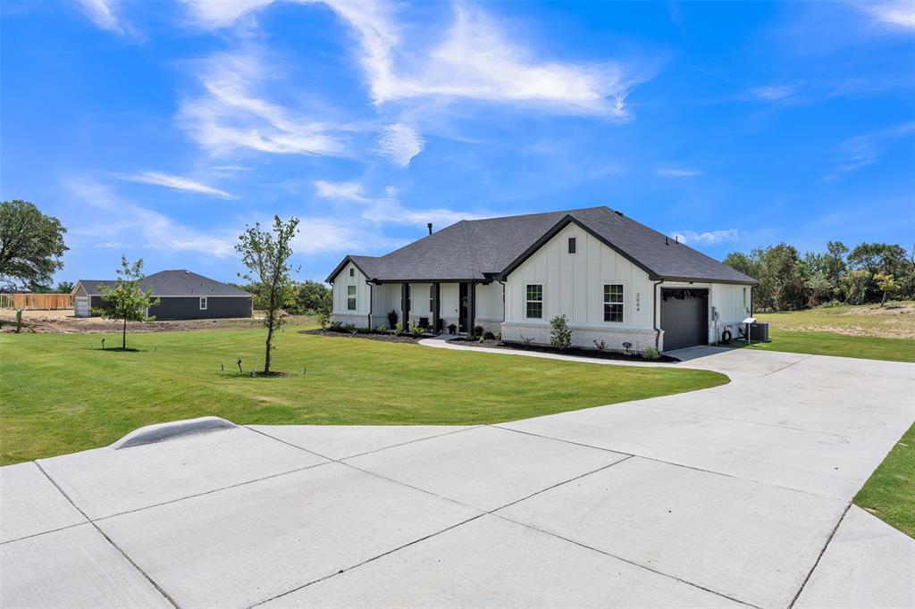 2004 Willy Dilly Road Springtown, TX 76082 - Photo 4 of 40 Modern farmhouse-style exterior featuring white board-and-batten siding with dark trim, a dark shingle roof, an attached garage with a dark door, and a concrete driveway