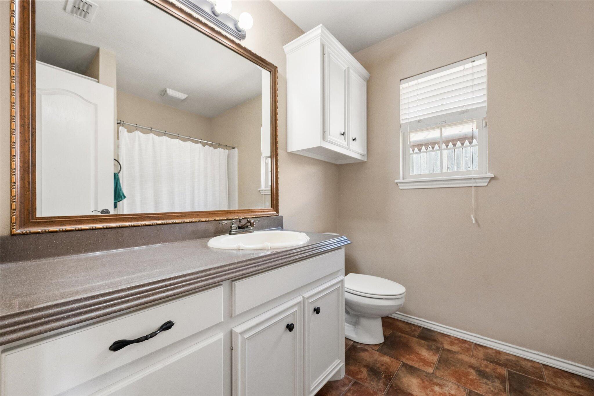 5704 107th Street Lubbock, TX 79424 - Photo 29 of 36 a bathroom with a granite countertop sink a toilet and a window
