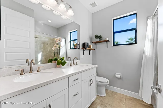 a bathroom with a double vanity sink toilet mirror and window