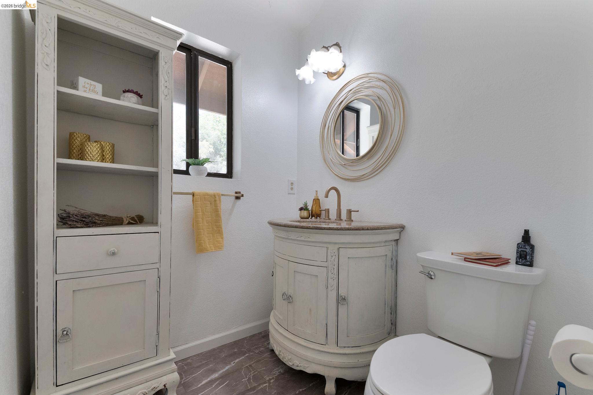 22963 Robertson Ranch Road Sonora, CA 95370 - Photo 20 of 90 Bathroom featuring a round vanity mirror, a vanity with a countertop sink and brass-finish faucet, and a toilet