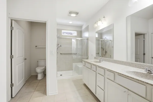 a spacious bathroom with a granite countertop toilet a double vanity sink a mirror and a shower