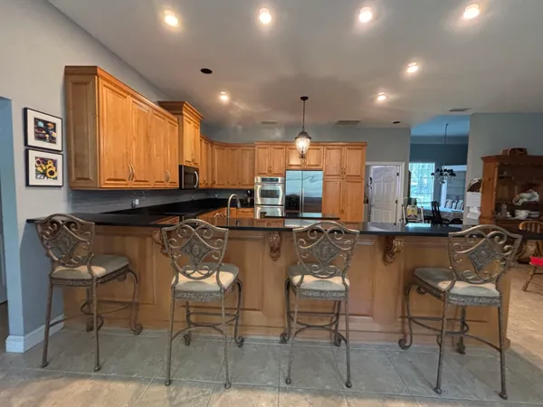 a kitchen with stainless steel appliances granite countertop a stove top oven a sink a refrigerator and chairs