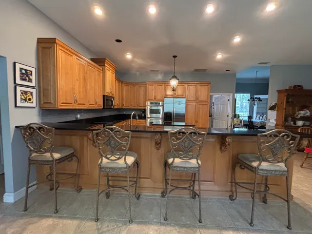 a kitchen with stainless steel appliances granite countertop a stove top oven a sink a refrigerator and chairs