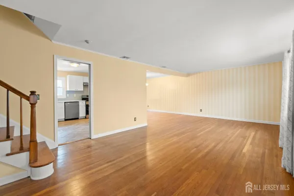 a view of empty room with wooden floor and kitchen