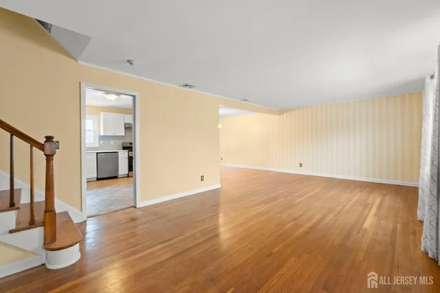 a view of empty room with wooden floor and kitchen