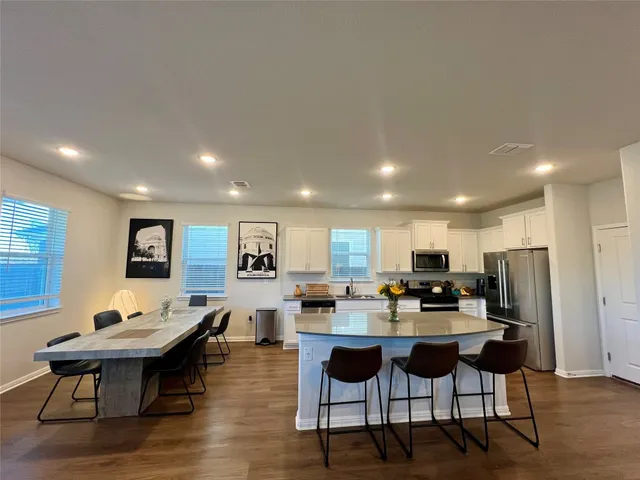 a living room with stainless steel appliances kitchen island granite countertop a dining table chairs and a refrigerator