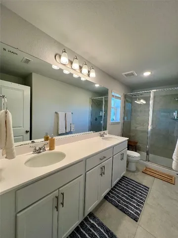 a spacious bathroom with a double vanity sink a toilet a mirror and shower