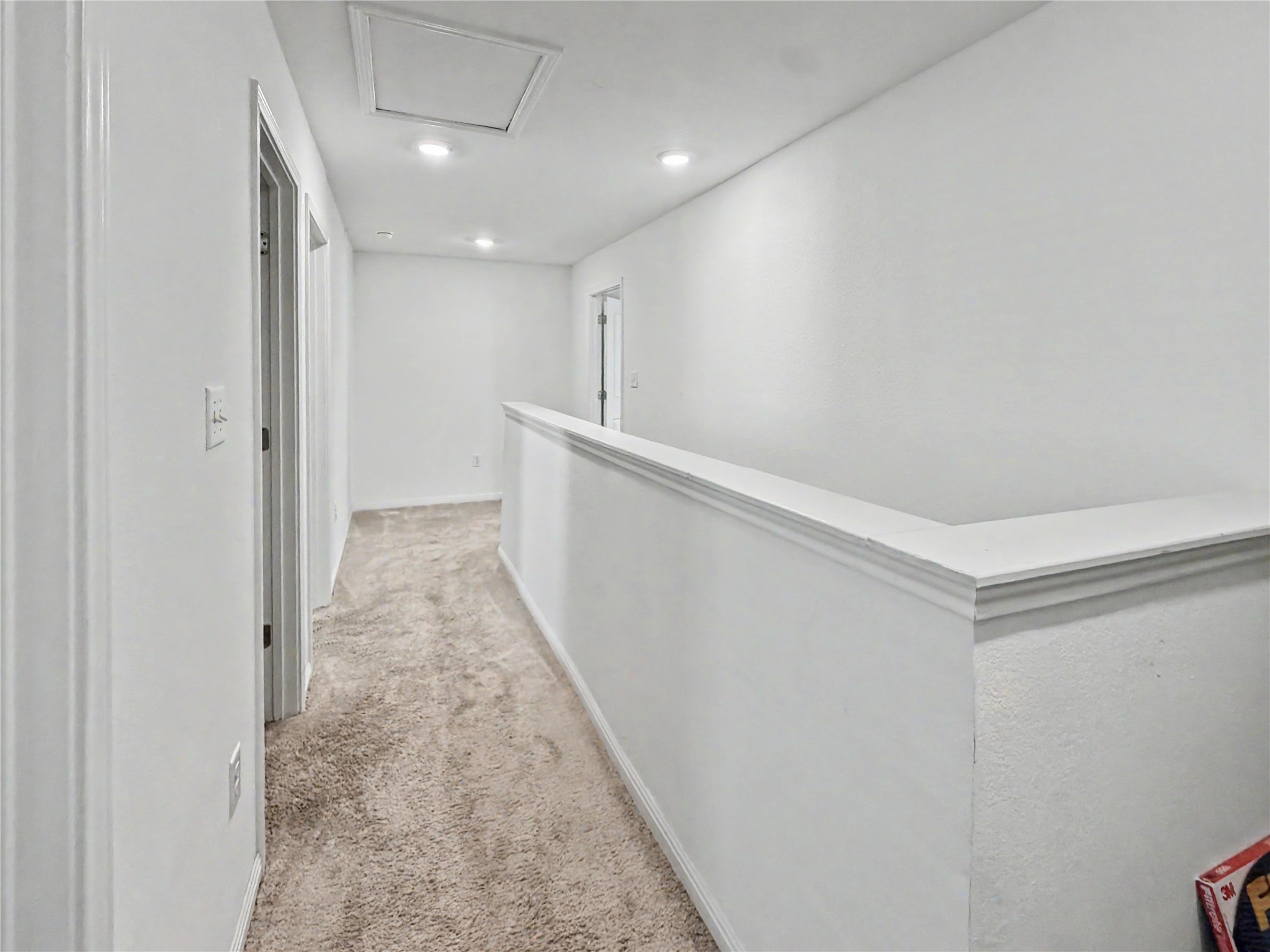 Recessed lighting illuminates a long upstairs hallway lined with soft plush carpeting.