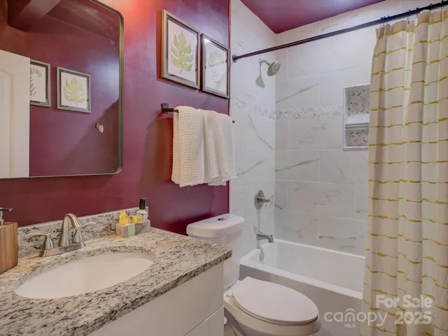 a bathroom with a granite countertop bathtub shower sink vanity mirror and toilet