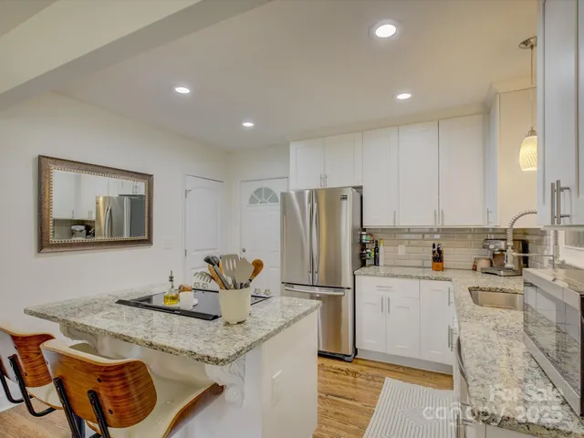 a kitchen with stainless steel appliances granite countertop a sink a stove a refrigerator and white cabinets