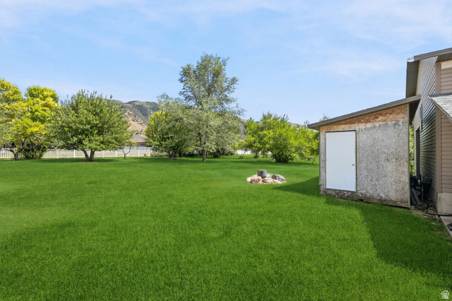 580 North 300 East Logan, UT 84321 - Photo 70 of 74 Expansive green lawn with a white picket fence, mature trees, mountain backdrop, and an attached storage shed