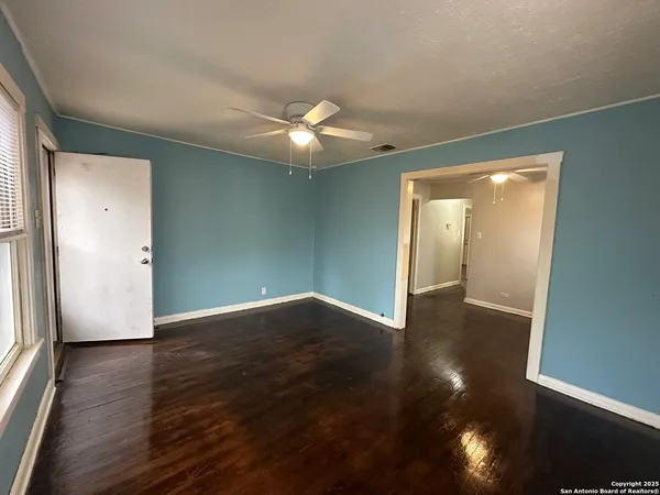 an empty room with wooden floor chandelier fan and windows