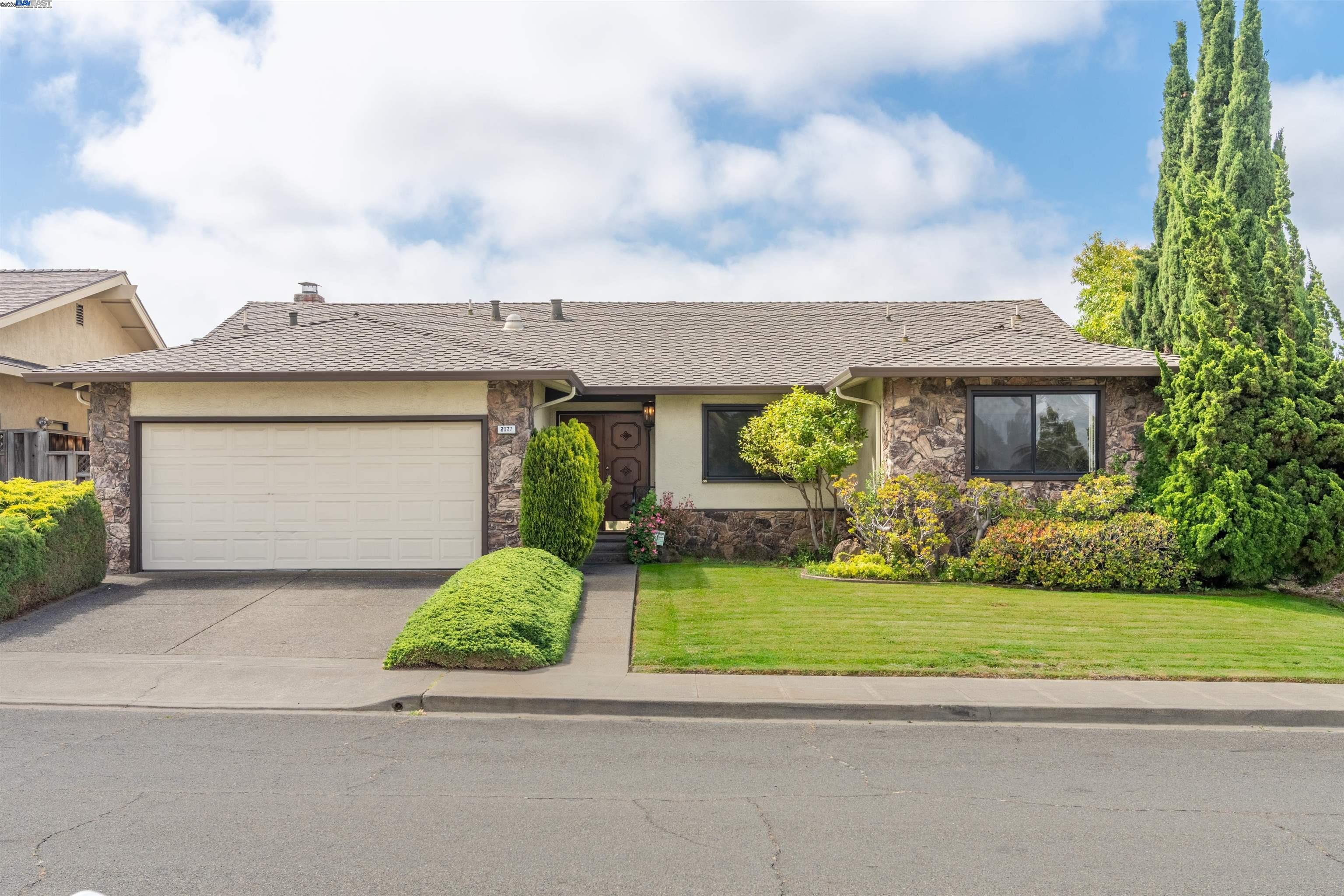 a view of a white house next to a yard with plants and large trees