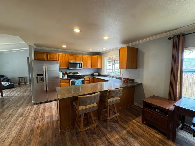 a kitchen with stainless steel appliances granite countertop a refrigerator a stove a sink dishwasher and a dining table with wooden floor