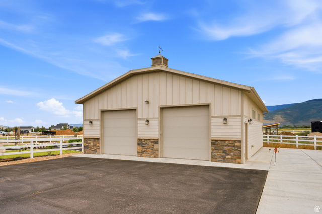 560 Aspen Road Francis, UT 84036 - Photo 12 of 59 Modern agricultural garage featuring two oversized bay doors with steel frames, stone veneer accents along the foundation, standing-seam metal siding in neutral tones, and a peaked roofline with cupola detail