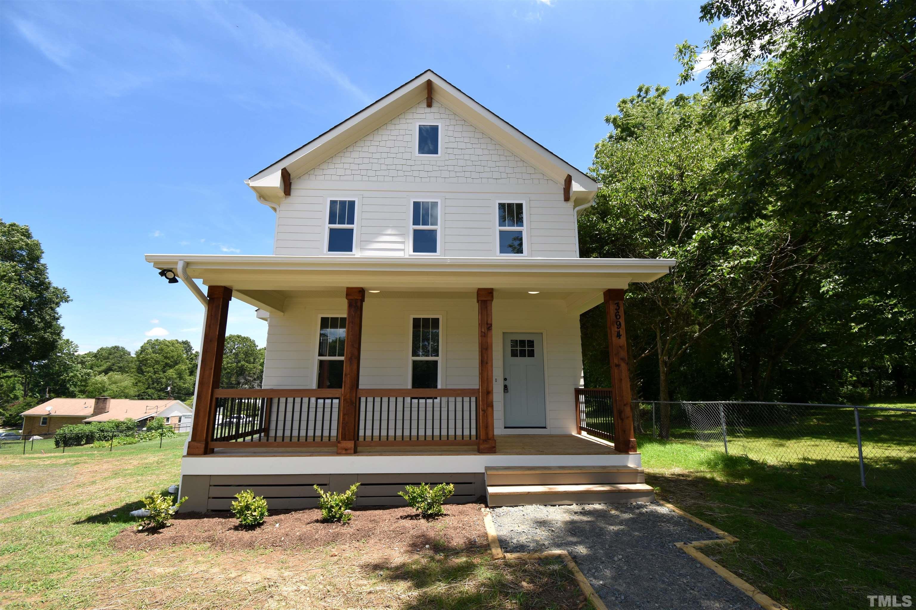 a view of a white house with a small yard and large trees