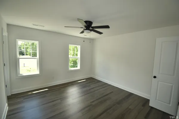 an empty room with wooden floor ceiling fan and windows