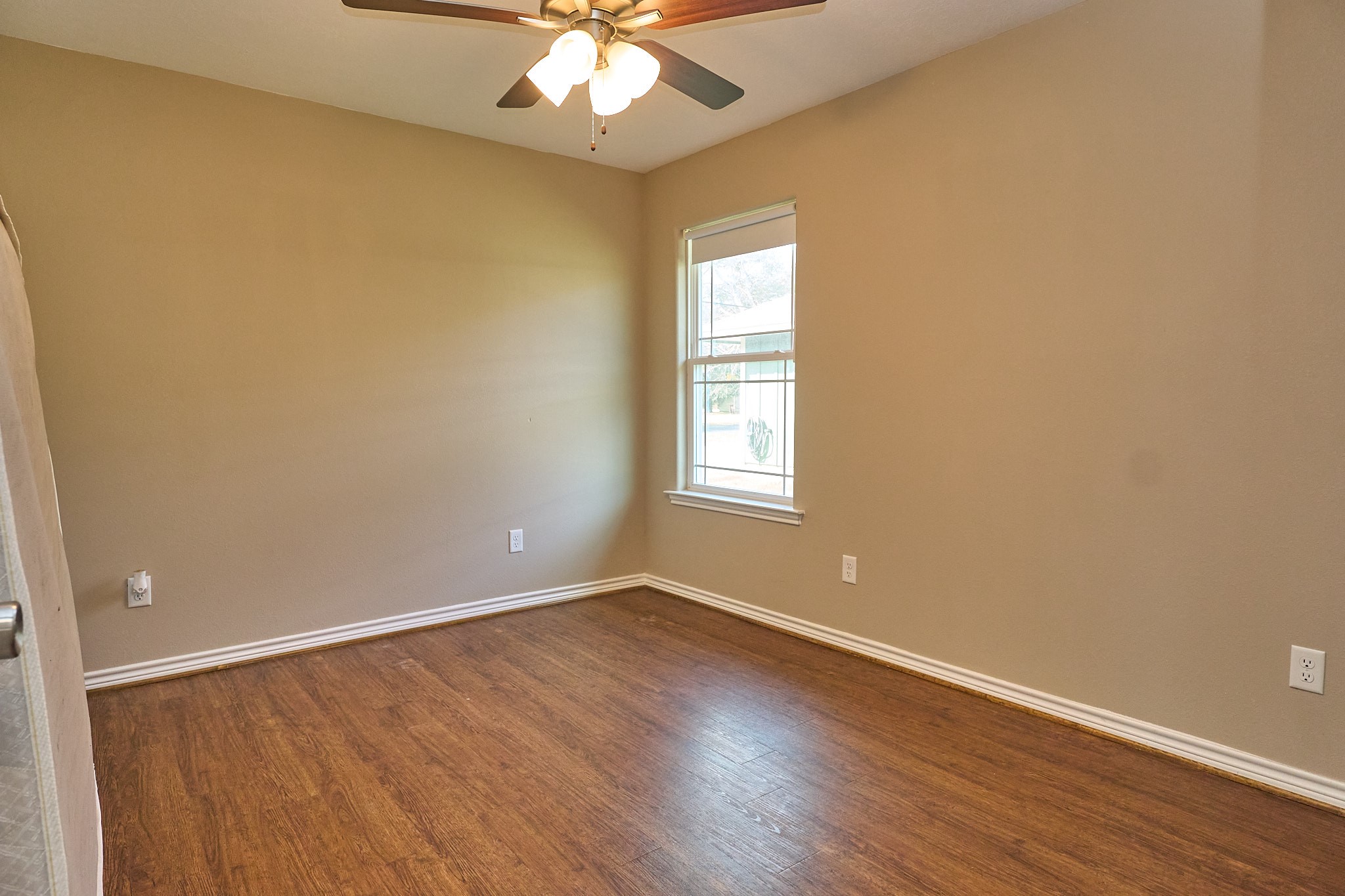 1807 Nuches Lane Bryan, TX 77803 - Photo 18 of 27 This room features warm wood flooring, neutral walls, a ceiling fan, and a window for natural light, creating a cozy and inviting space.