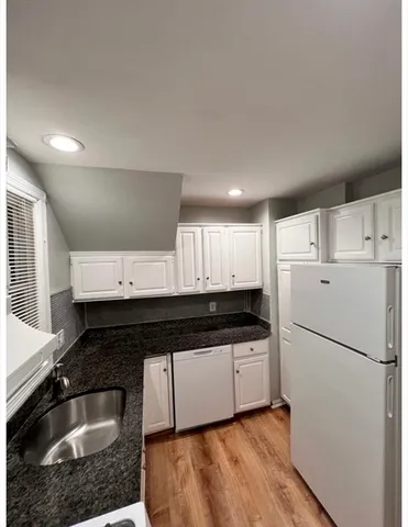 a kitchen with granite countertop a refrigerator sink and white cabinets
