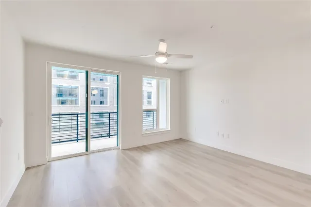 an empty room with wooden floor and windows with curtains