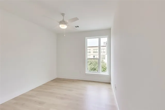 an empty room with wooden floor chandelier fan and windows