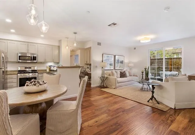 a kitchen with stainless steel appliances kitchen island granite countertop a stove a refrigerator a kitchen island a dining table and chairs with wooden floor