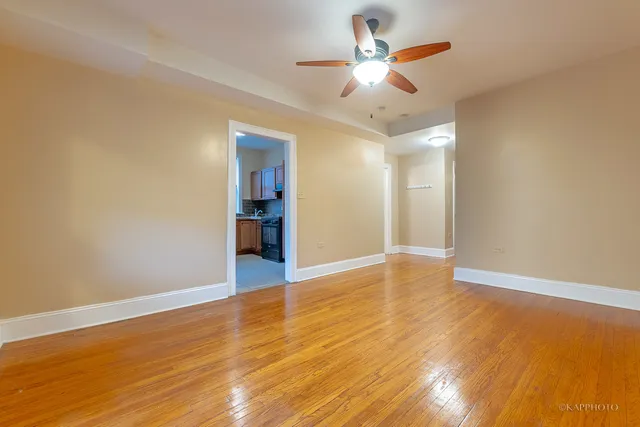 a view of an empty room with wooden floor and a ceiling fan