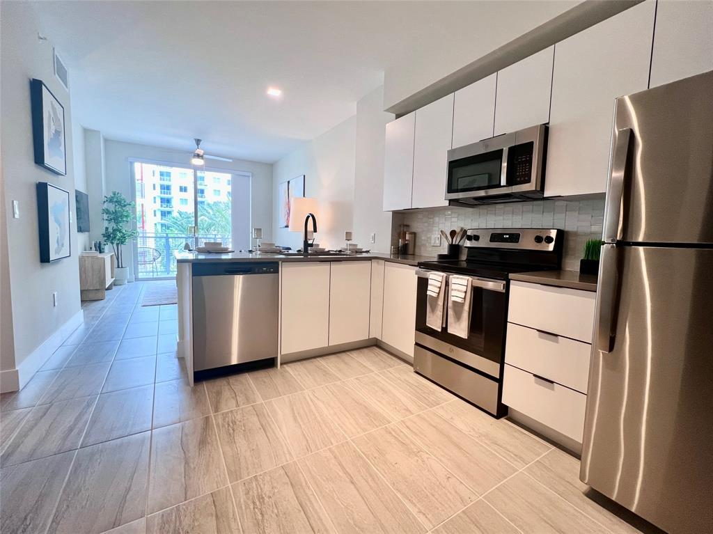 120 North Compass Way, Unit 230 Dania Beach, FL 33004 - Photo 5 of 42 a kitchen with stainless steel appliances granite countertop a refrigerator a stove top oven a sink dishwasher and white cabinets with wooden floor