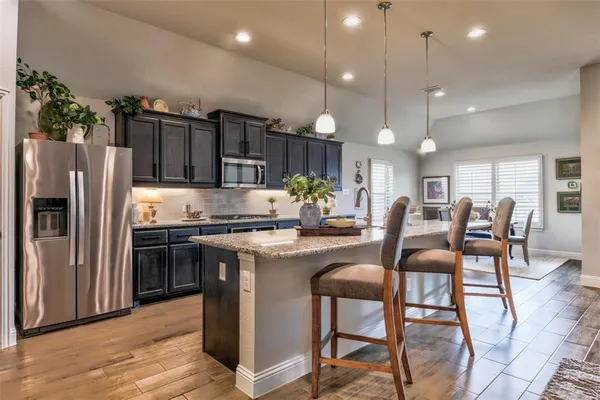 a kitchen with stainless steel appliances kitchen island granite countertop a refrigerator a stove a sink and a dining table with wooden floor