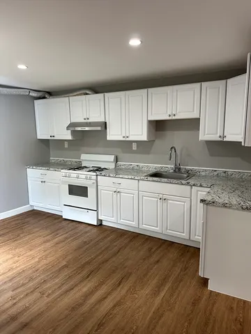 a kitchen with stainless steel appliances granite countertop a sink a stove a refrigerator and cabinets with wooden floor